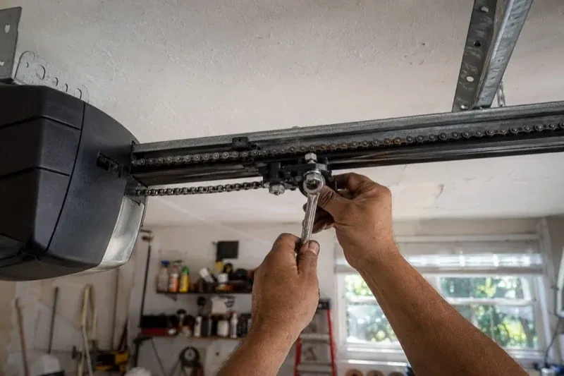 Hands holding a wrench against an opener trolley beneath a chain rail — Chain-Drive Opener Repair, Strathroy-Caradoc