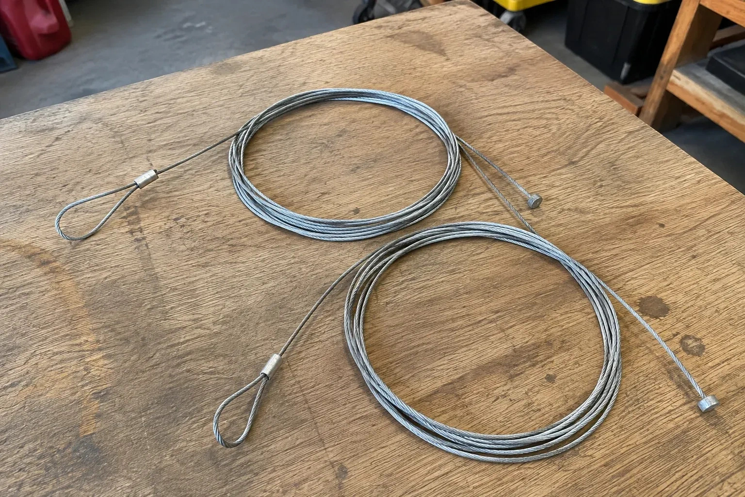 Two coiled steel cables with loop and stop ends on a workbench. — Garage Door Cable Replacement, Strathroy-Caradoc