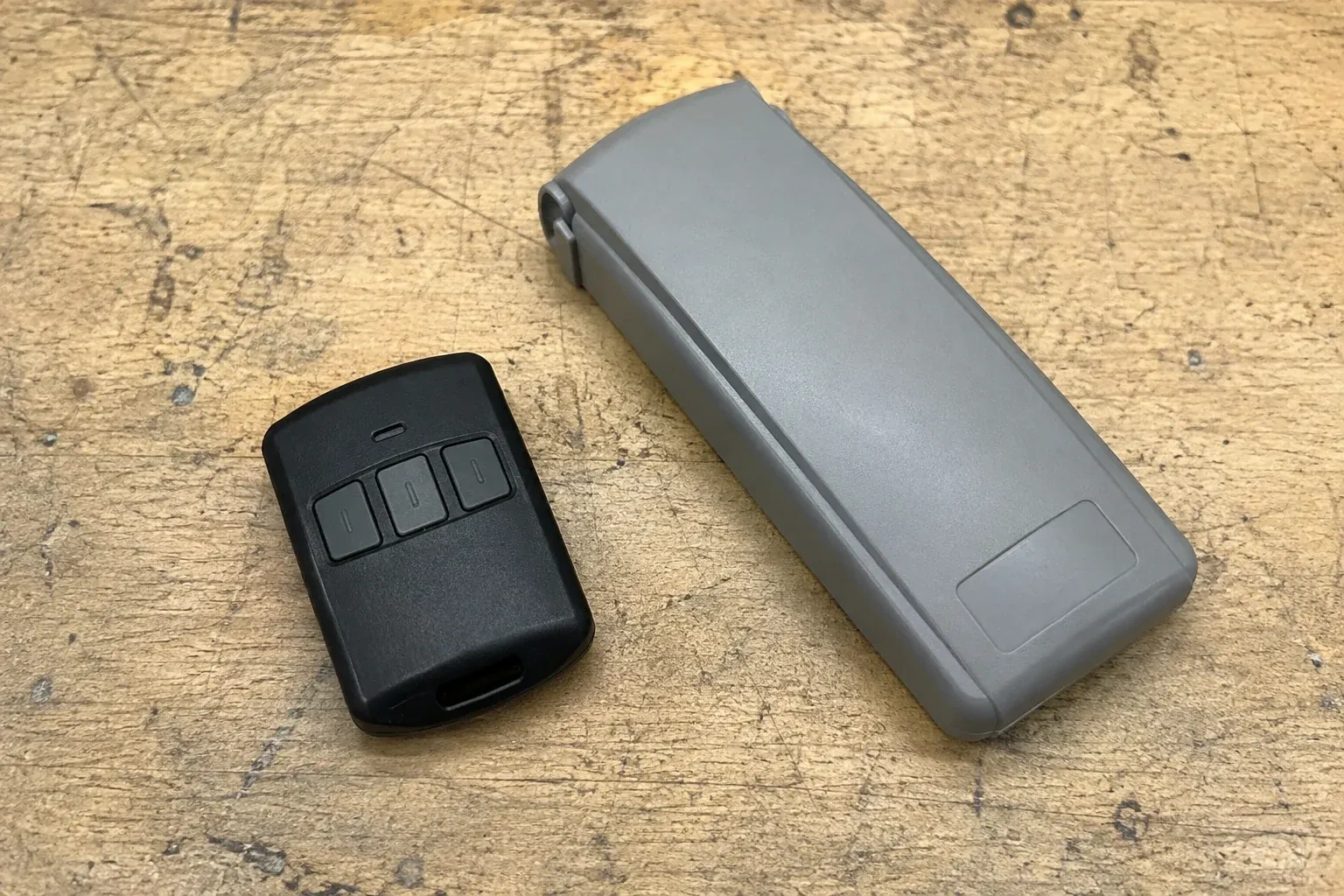 Three-button remote beside a closed grey keypad cover on a workbench. — Garage Door Remote and Keypad Programming, Strathroy-Caradoc
