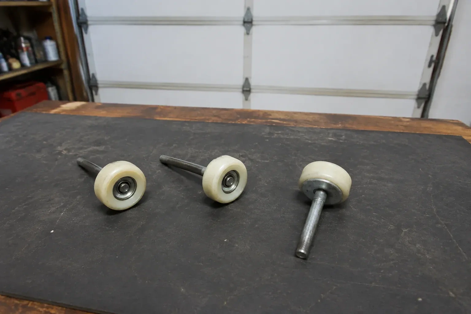 Three detached nylon-wheel garage door rollers with steel stems on a work mat. — Garage Door Roller Replacement, Strathroy-Caradoc